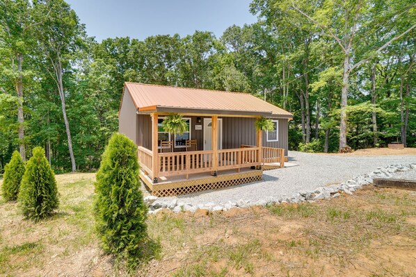 A cabin with a wooden deck, surrounded by trees and a gravel driveway.