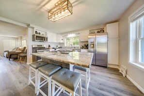 Une cuisine moderne avec des meubles blancs, un grand îlot central doté de tabourets, des appareils en acier inoxydable et un luminaire suspendu.