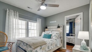 A bedroom with a bed, a chair, a nightstand, a ceiling fan, and a sign that reads "BEACH HOUSE". - Walk to Water: Coastal-chic Home Near Myrtle Beach (North Myrtle Beach)