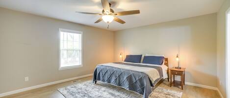 A bedroom with a bed, a ceiling fan, a nightstand, and a window.