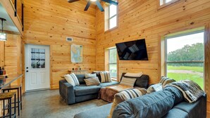 Ein gemütliches Blockhaus-Interieur mit einer Eckcouch, einem flachbildfernseher an der Wand und großen Fenstern mit Blick ins Freie.