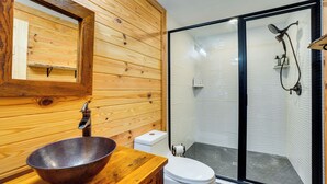 Ein Holzeinrichtung mit einem großen Holzbacche, einer weißen Toilette und einem durch eine Glaswand abgetrennten Duschbereich.