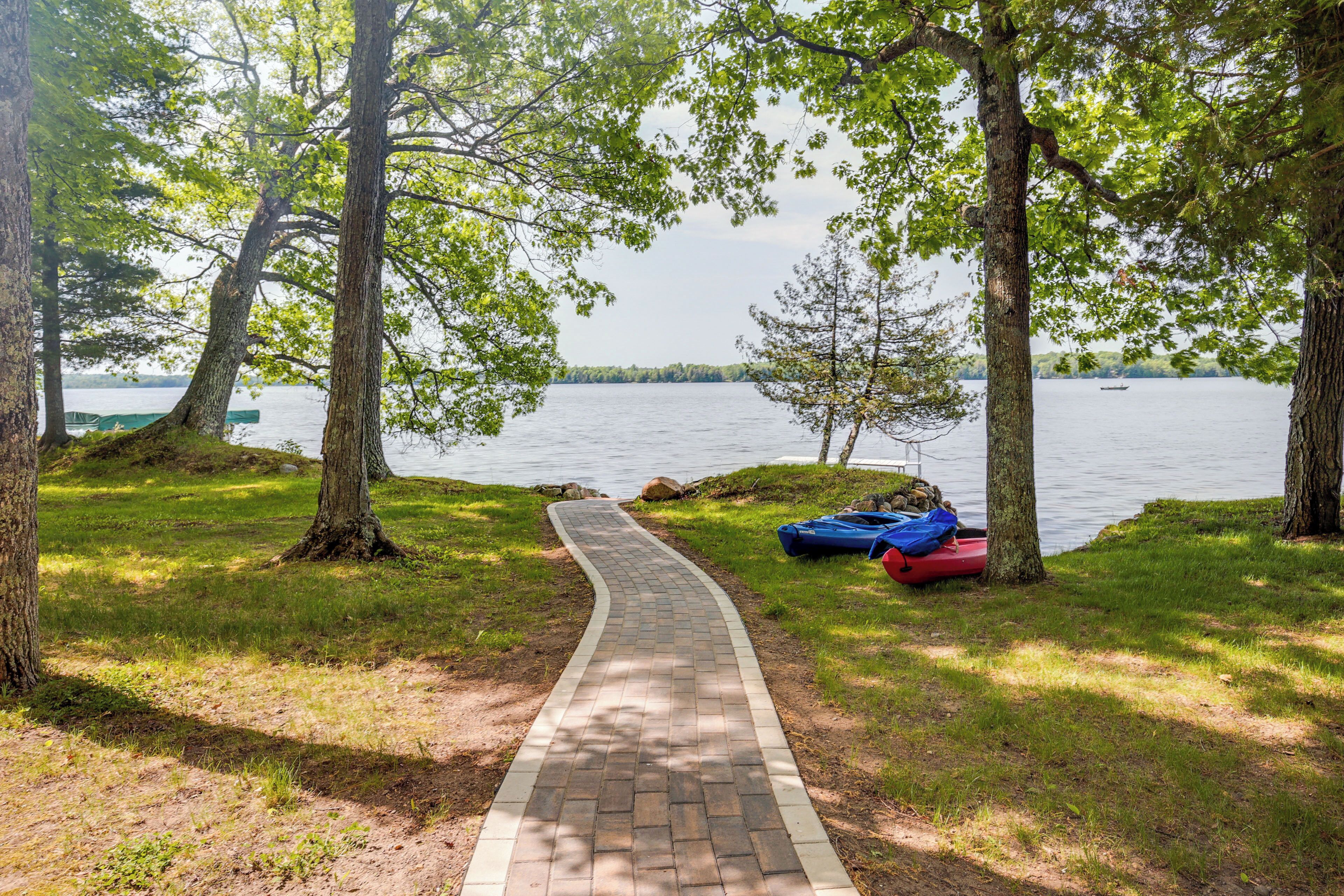 A paved pathway leading to a lake, surrounded by trees and a kayak.