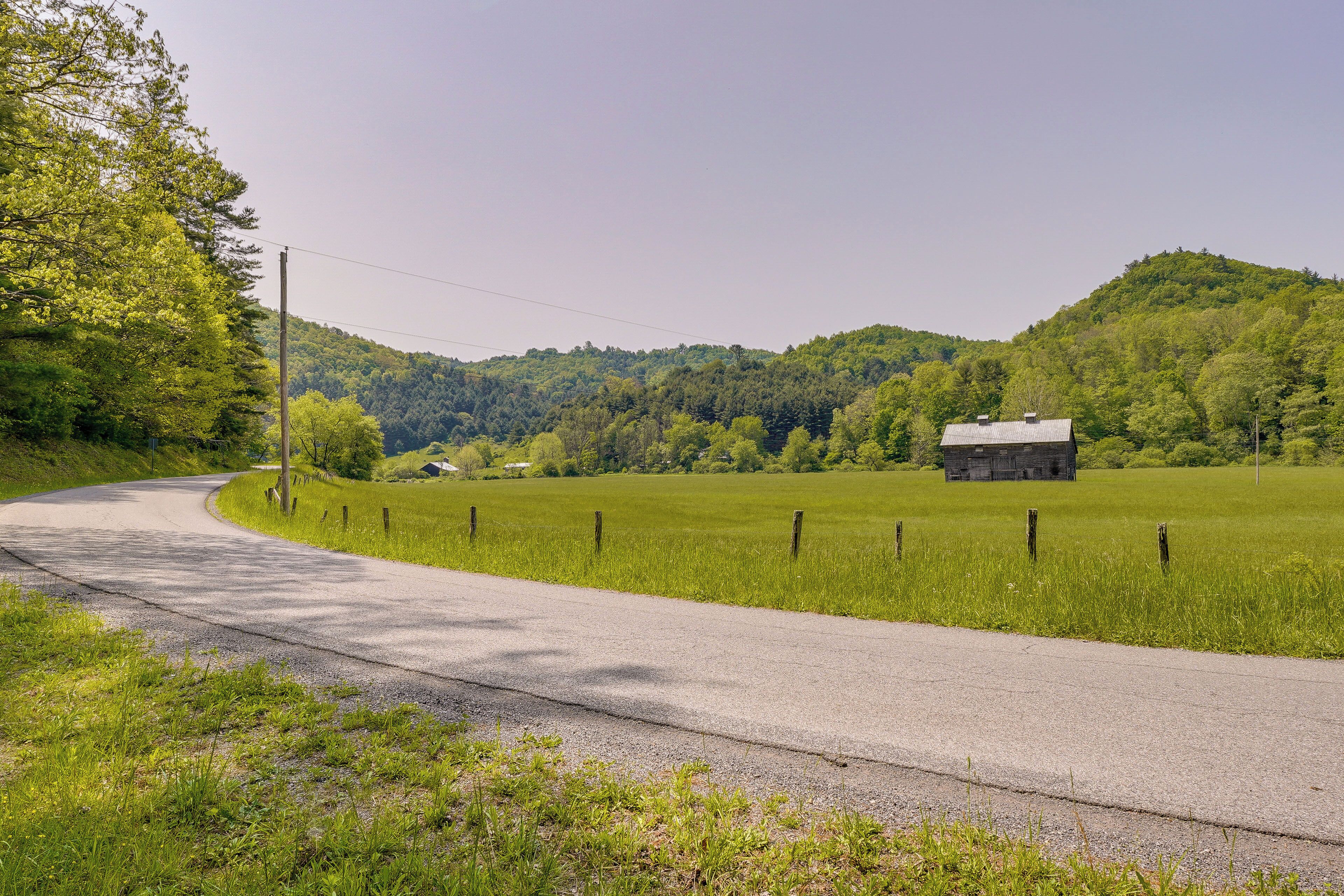 A rural road curving through a green landscape with a barn and open fields.