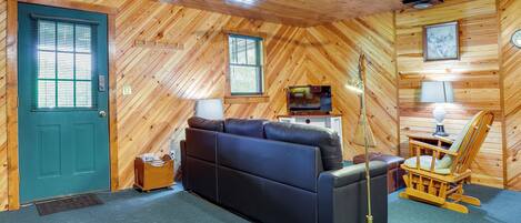 A wooden-paneled room with a green door, a black sofa, a wooden rocking chair, and a ceiling fan.
