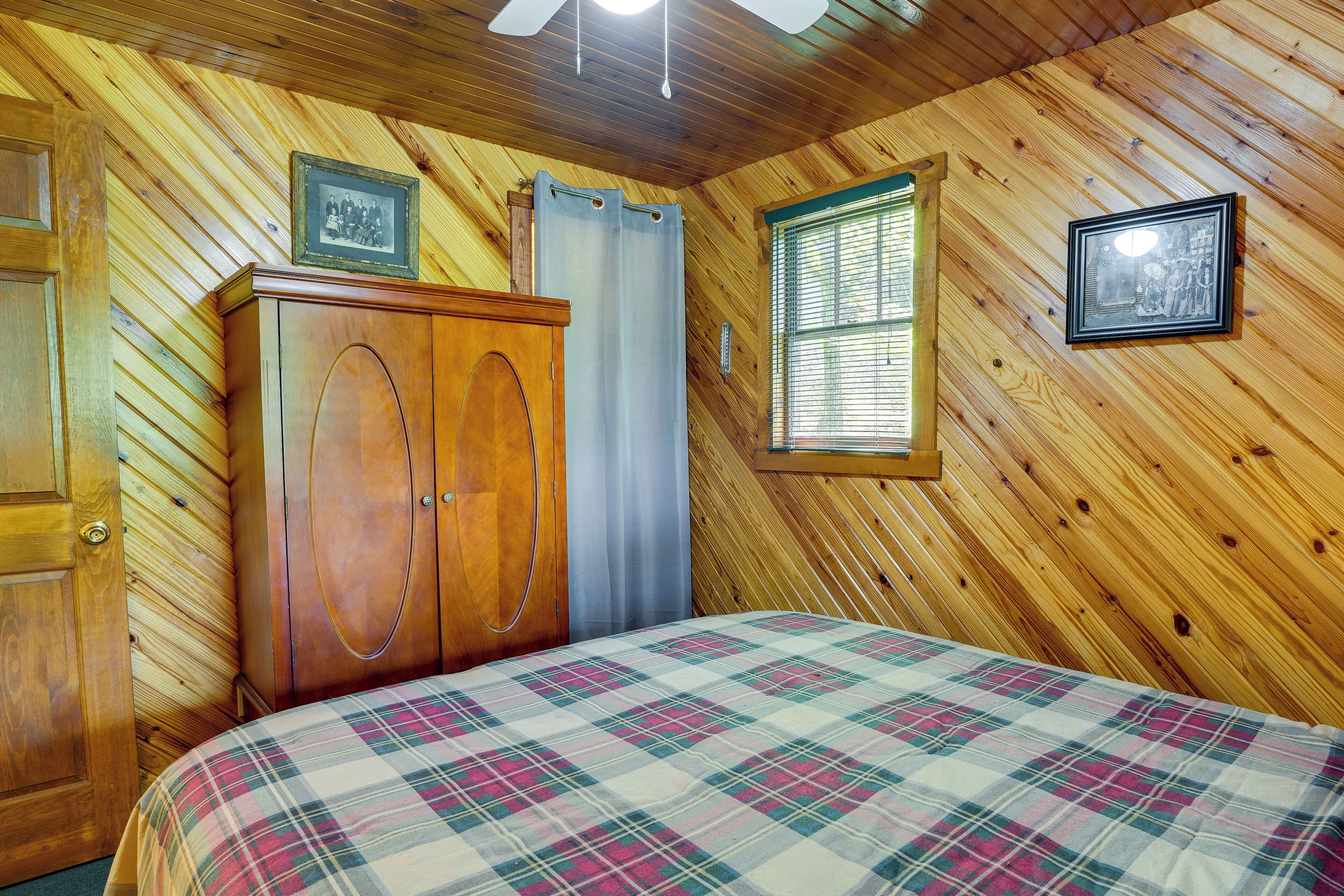 Um quarto com painéis de madeira, uma cama, um guarda-roupa de madeira, uma janela com persianas e duas molduras com quadros na parede.