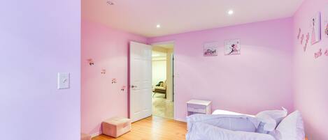 A pink-themed bedroom with a bed, a small bedside table, and a door leading to another room.