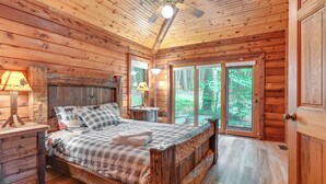 Camera da letto in una baita di legno, con un letto, comodini e una ventola a soffitto.