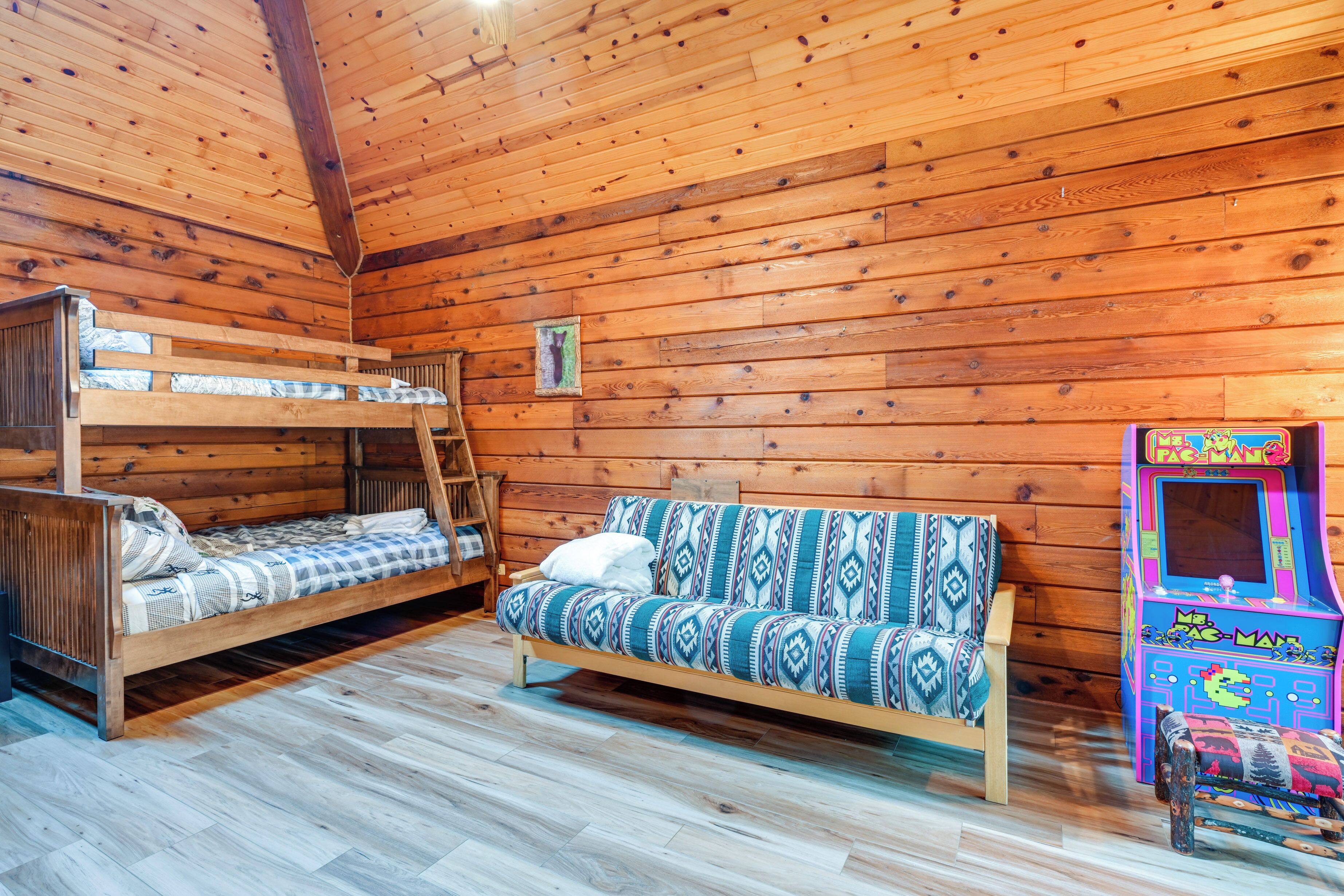 Une cabane aux murs et au plancher en bois, avec un lit superposé, un canapé et une borne d’arcade aux couleurs vives.