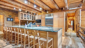 Interno di una baita in legno con cucina, caratterizzata da un'isola centrale con sgabelli da bar, armadi a incasso e un frigorifero in acciaio inox.