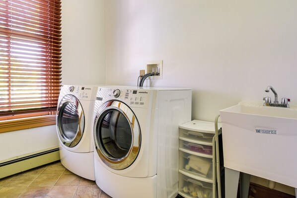 A laundry area with two front-loading washing machines, a sink, and a drying rack.