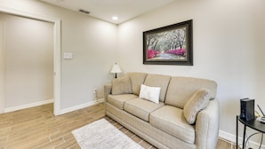 Ein Wohnzimmer mit beigefarbenem Sofa, einem weißen Teppich, einem gerahmten Bild an der Wand und einer Lampe.