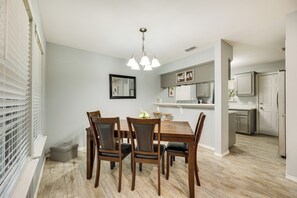 A dining area with a wooden table and chairs, a chandelier, and a kitchen in the background. - Fenced Yard & Grill: San Juan Vacation Rental! (San Juan)