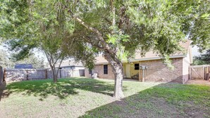 A backyard with a tree, a brick house, and a wooden fence. - Fenced Yard & Grill: San Juan Vacation Rental! (San Juan)