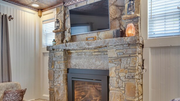 A stone fireplace with a TV mounted above it, a stone shelf with a lantern, and a cozy seating area with a cushioned chair and a decorative pillow.