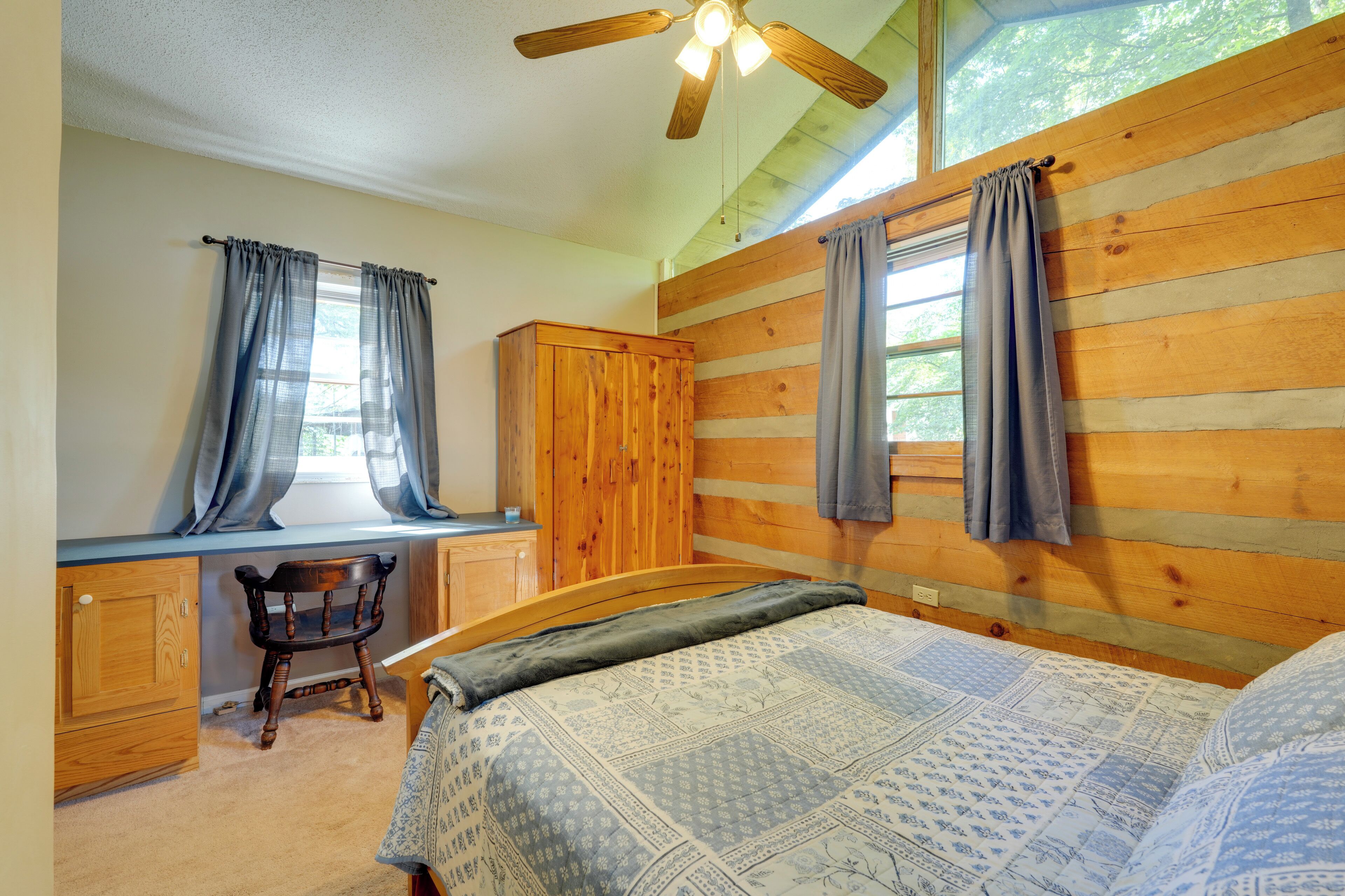 A bedroom with a wooden headboard, a bed with patterned bedding, a desk with a chair, and a wardrobe.