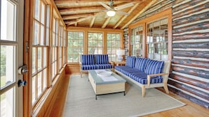 Ein Holzblockhaus-Interieur mit Holzbalkendecke, großen Fenstern, einem Deckenventilator und blau gestreifter Möbel.