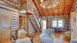 Ein Holzblockhaus-Interieur mit einer Holztreppe, einer Chandelüster, einer Essecke und einem Kamin.