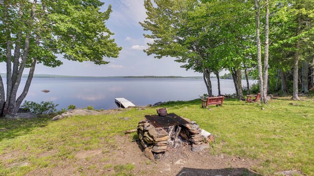 Um camping à beira do lago com lareira, bancos e uma barraca.