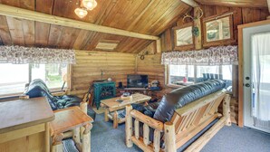 Interior de cabana com teto de madeira, sofá, televisão e mesa de jantar.