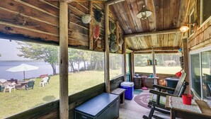 Quarto rústico de madeira com um banco, uma mesa e vista para uma área gramada com mobiliário de exterior.