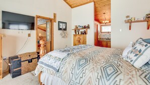 A bedroom with a large bed, wooden ceiling beams, a television, a wooden cabinet, and a dresser.