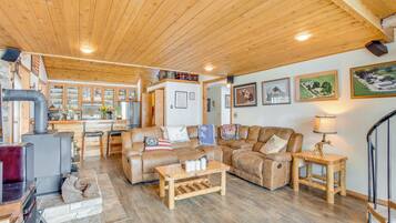 A cozy living room with a fireplace, wooden furniture, and a kitchen in the background.