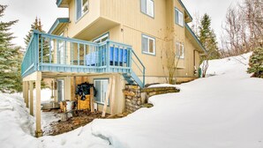 A two-story house with a blue balcony, a stone foundation, and a snow-covered yard.