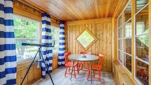 A wooden cabin interior with a telescope, a round table with chairs, and large windows. - Charming Michigan Cottage w/ Sunroom & Lake Access (Hubbard Lake)