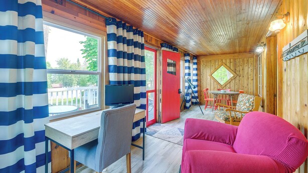 A cozy cabin interior with a wooden ceiling, a desk with a chair, a red door, and a pink sofa. - Charming Michigan Cottage w/ Sunroom & Lake Access (Hubbard Lake)