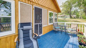 A wooden deck with a blue floor, a reclining chair, a table with chairs, and a view of the surrounding area. - Charming Michigan Cottage w/ Sunroom & Lake Access (Hubbard Lake)