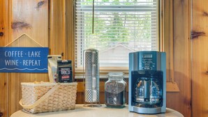 A coffee station with a coffee maker, a basket, a jar, and a sign reading "Coffee - Lake Wine - Repeat". - Charming Michigan Cottage w/ Sunroom & Lake Access (Hubbard Lake)