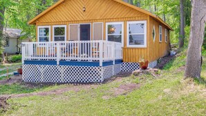 A wooden cabin with a white porch and multiple windows, surrounded by trees. - Charming Michigan Cottage w/ Sunroom & Lake Access (Hubbard Lake)