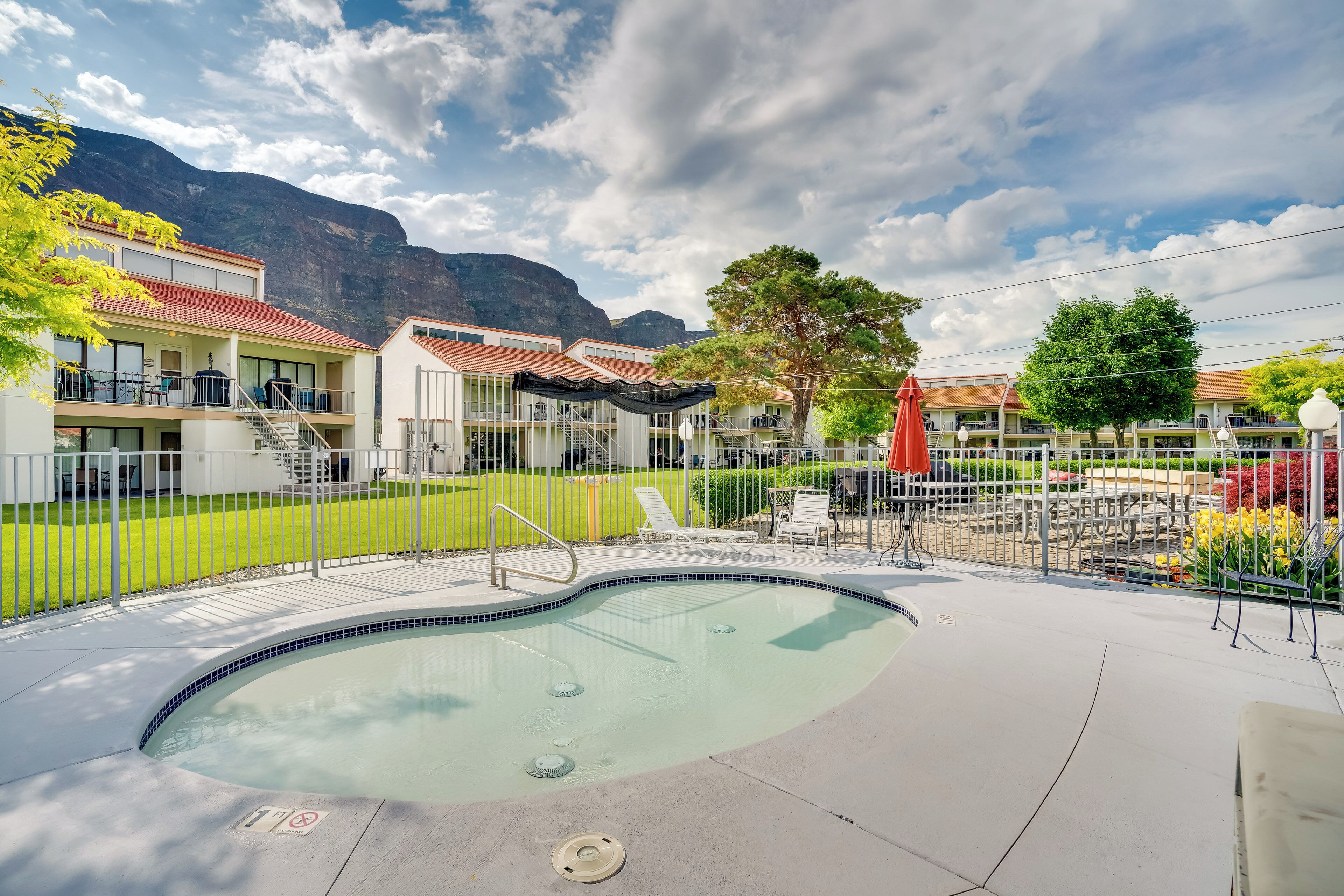 A swimming pool with a tiled edge, surrounded by a fence, and a view of mountains in the background.