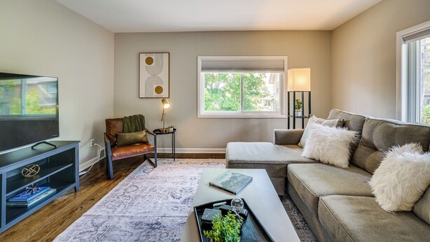 A living room with a sofa, a coffee table, a TV, and a window with a view of trees. - Top-floor Wyandotte Apt Near Detroit Riverfront! (Wyandotte)