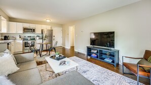 A modern living room with a sofa, coffee table, and a TV. There is a kitchen area with cabinets and appliances. - Top-floor Wyandotte Apt Near Detroit Riverfront! (Wyandotte)
