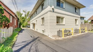 A two-story residential building with a light blue exterior, a front yard with a wooden fence, and a paved driveway. - Top-floor Wyandotte Apt Near Detroit Riverfront! (Wyandotte)