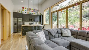 Et moderne køkken med spiseområde, en stor grå hjørnesofa og udsigt til et bjergrigt landskab gennem store vinduer.