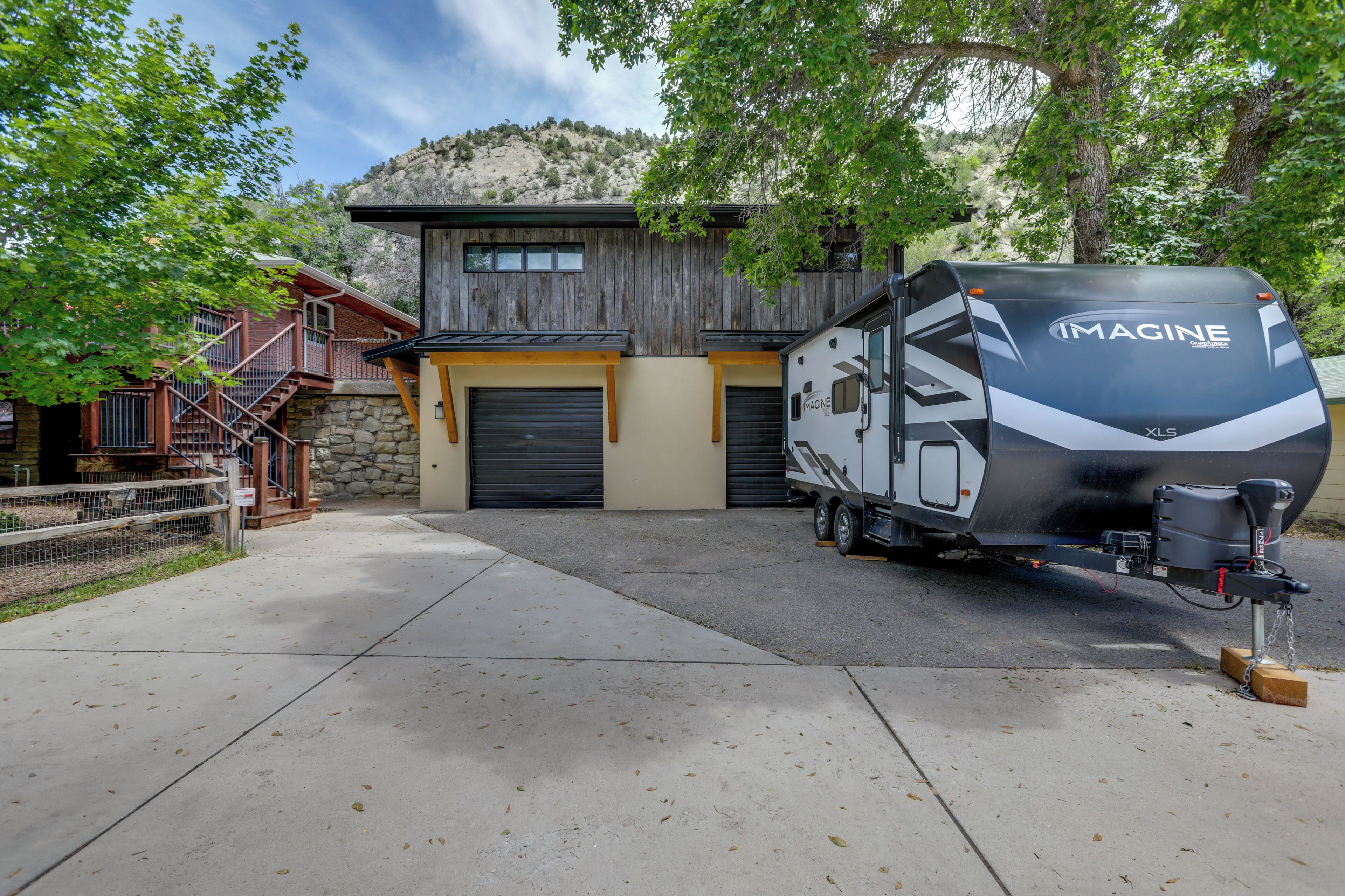 A modern RV with 'IMAGINE' branding parked in front of a rustic building with a stone facade and wooden accents.