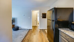 Una cocina con un refrigerador negro, piso de madera y una puerta blanca que da a otra habitación.