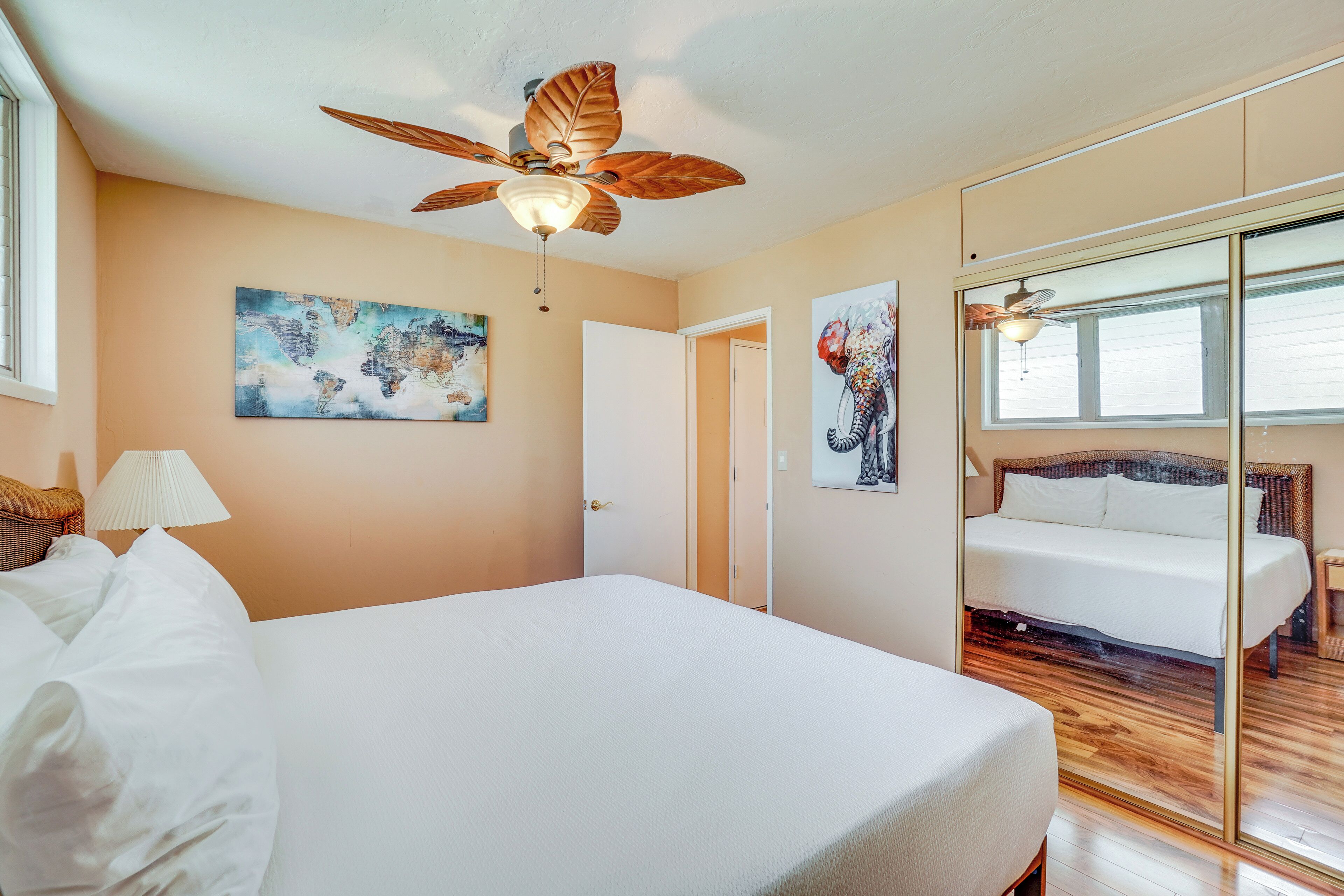 A bedroom with a large bed, a ceiling fan, a world map painting, and a window with blinds.