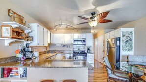Una cocina moderna con armarios blancos, una isla central con taburetes, un ventilador de techo y un comedor con mantel estampado.