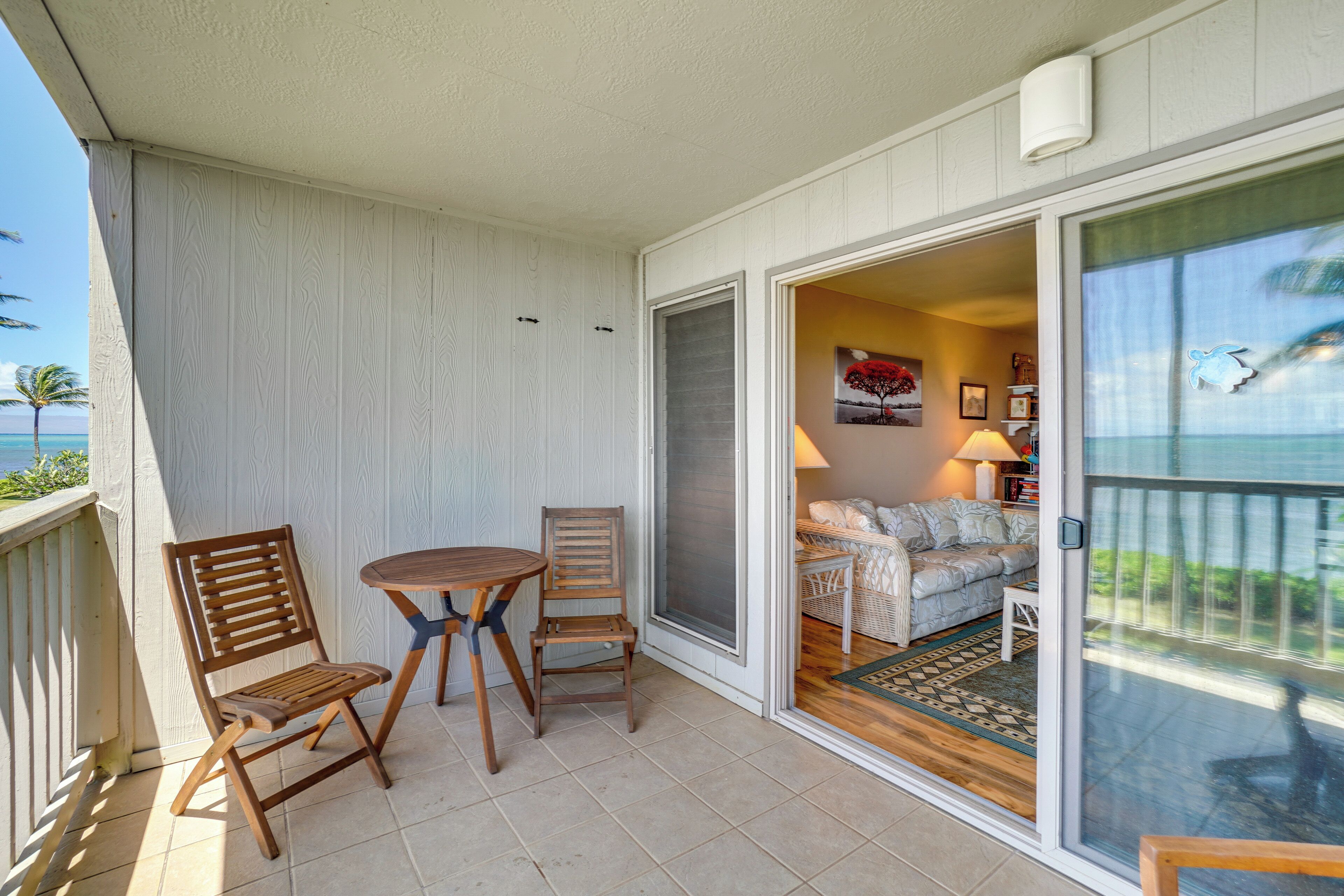 A balcony with a table and chairs, a sliding glass door leading to a living area with a sofa and a lamp.