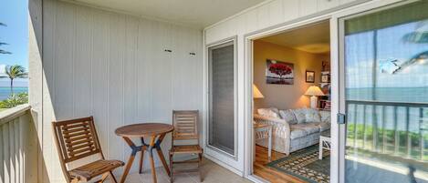 A balcony with a table and chairs, a sliding glass door leading to a living area with a sofa and a lamp.