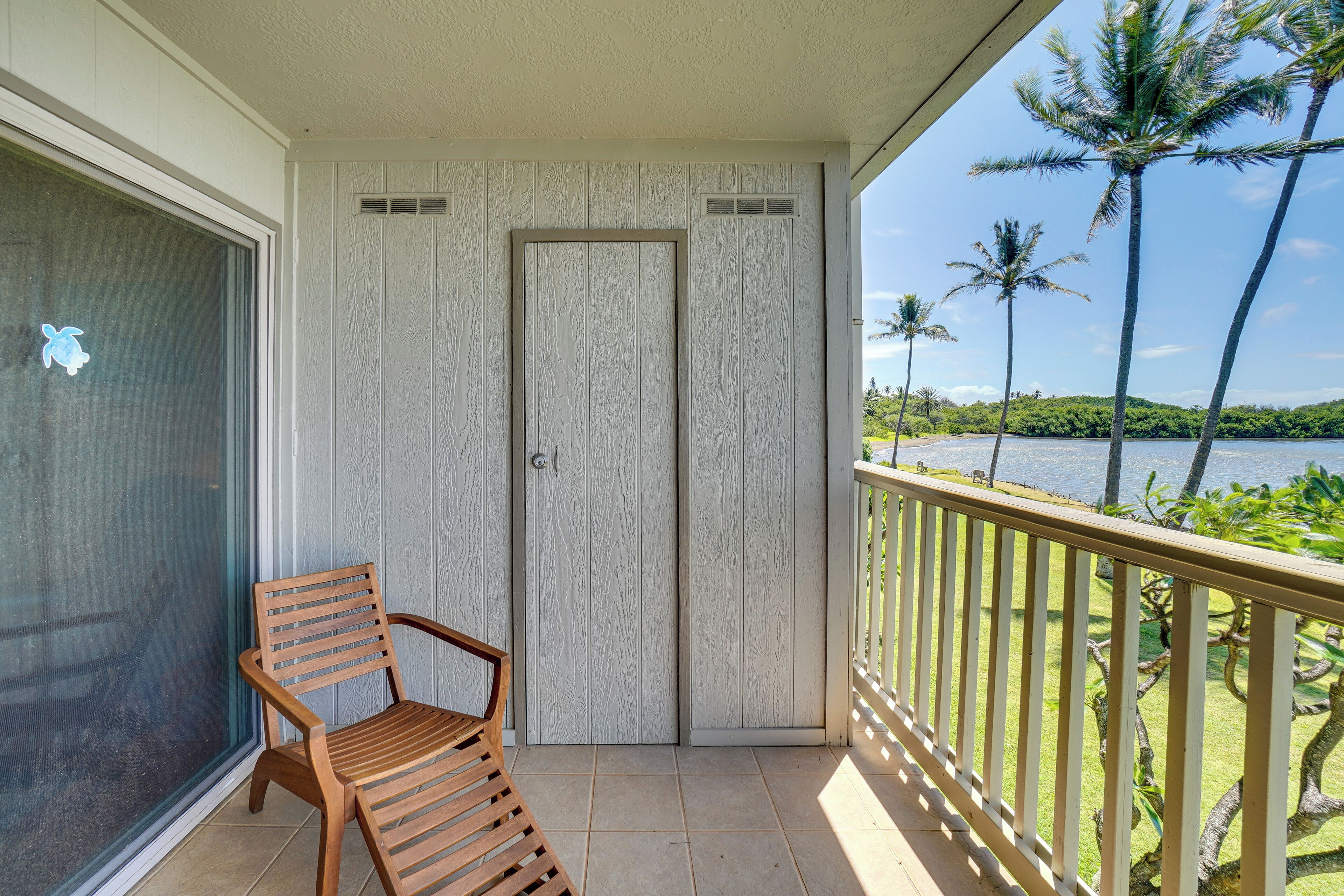 A wooden chair on a balcony with a view of palm trees and a body of water.