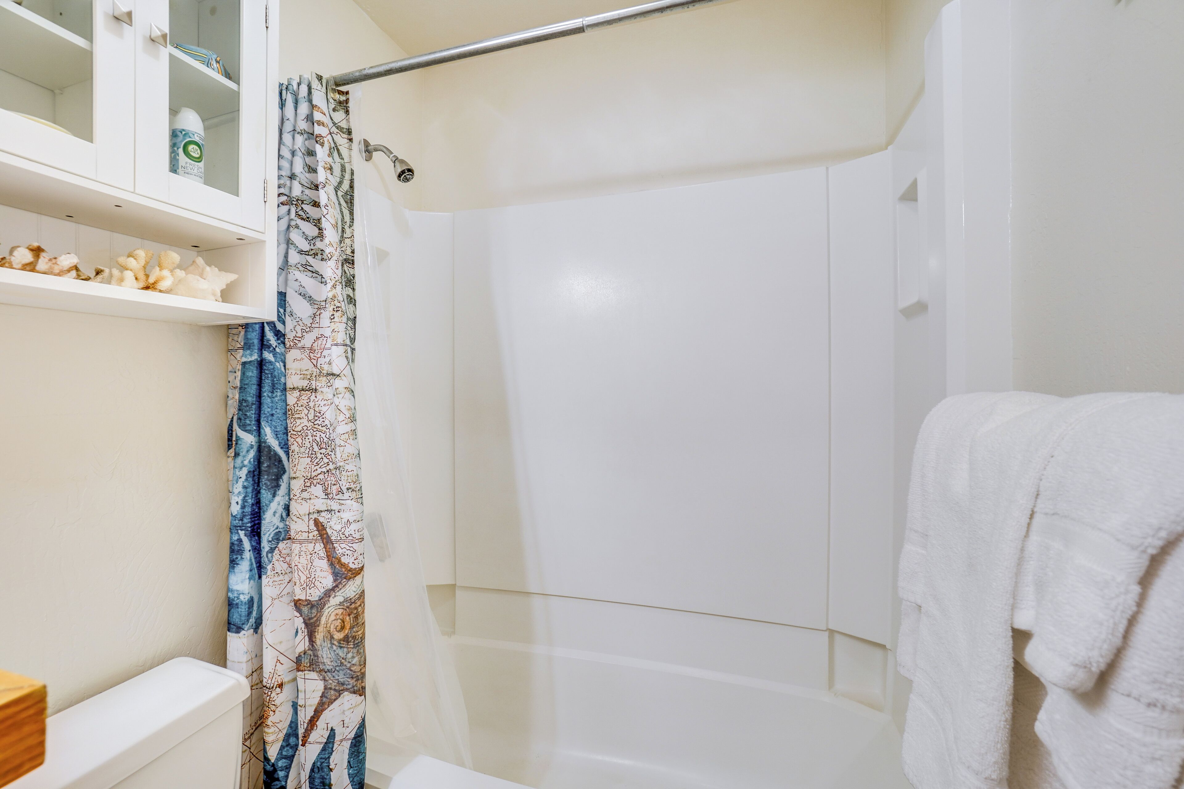 Un baño con cabina de ducha de vidrio, una bañera blanca, una toalla blanca colgada en la pared y un estante con artículos de aseo.