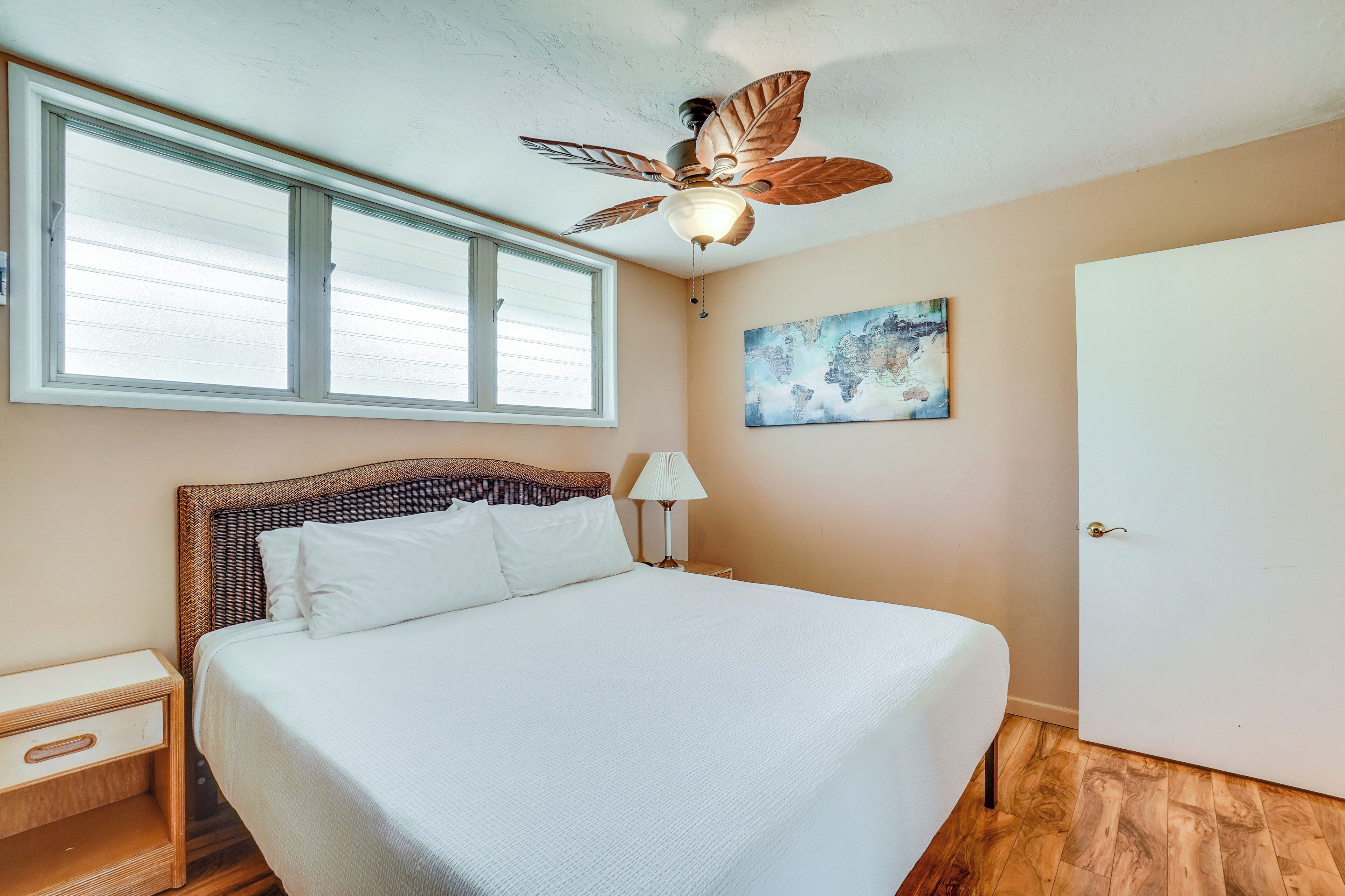 A bedroom with a bed, a ceiling fan, a window, a nightstand, a lamp, and a door.