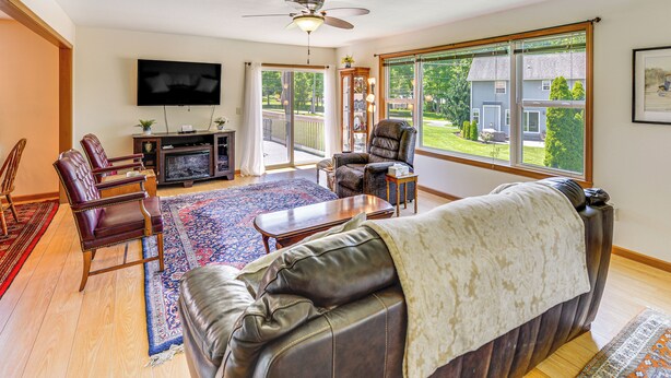 A living room with a leather sofa, a TV, and a large window offering a view of a house and greenery. - Wfh-friendly Columbiana Vacation Rental w/ Deck! (Columbiana)
