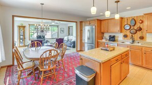 A kitchen with wooden cabinets, a stainless steel refrigerator, a dining area with a table and chairs, and a patterned rug. - Wfh-friendly Columbiana Vacation Rental w/ Deck! (Columbiana)