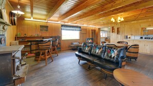 L’intérieur d’un chalet rustique, avec un plafond en bois, un canapé en cuir, des chaises en bois, un coin bar et une cuisine.